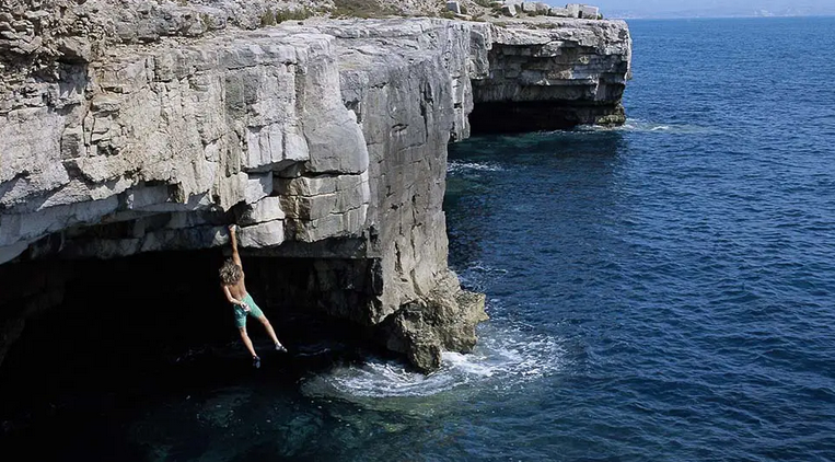 Climber traversing limestone sea cliffs above deep blue water